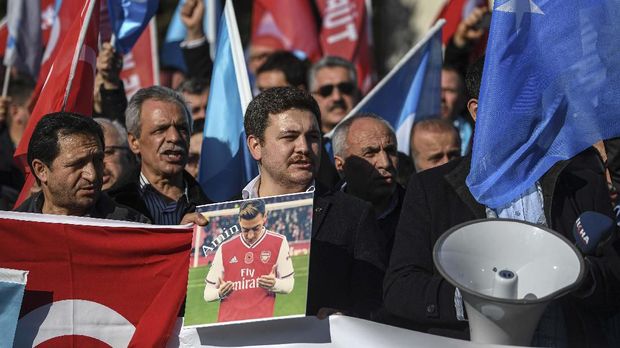 A supporter of China's Muslim Uighur minority holds a placard of Arsenal's Turkish origin German midfielder Mesut Ozil past East Turkestan flags during a demonstration at Beyazid square in Istanbul on December 14, 2019. - Arsenal's Mesut Ozil, a German footballer of Turkish origin, expressed on December 14, 2019 support for Uighurs in Xinjiang and criticised Muslim countries for their failure to speak up for them. (Photo by Ozan KOSE / AFP)
