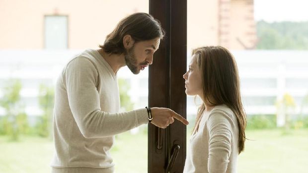 Unhappy young couple arguing standing at house door, angry husband pointing at wife blaming her of problems, conflicts in marriage, bad relationships, man and woman having quarrel or disagreement
