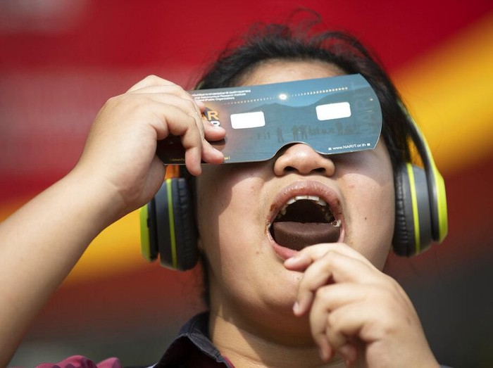 A student holds a special filter to observe a solar eclipse while eating an ice cream treat at a school in Bangkok, Thailand, Thursday, Dec. 26, 2019. (AP Photo/Sakchai Lalit)