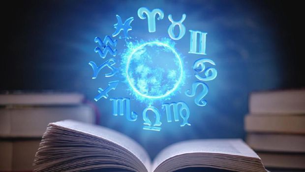 Open book on astrology on a dark background. The glowing magical globe with signs of the zodiac in the blue light. Concept of prediction and magic