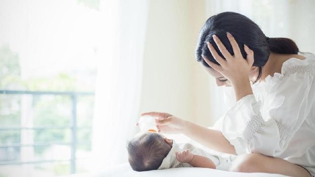 Asian Mother nursery feeding bottle of formula milk to newborn baby in bed suffering from post natal depression. Health care single mom motherhood stressful concept.