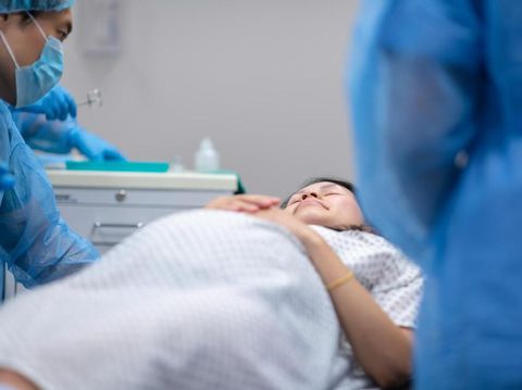 A pregnant woman is going in to surgery. She is laying on an operating table in the hospital's operating room. Surgeons surround the bed preparing for the medical procedure.
