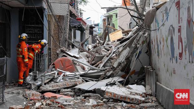 Reruntuhan ruko menimpa jalan kecil dan bagian depan rumah di sampingnya.