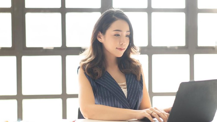 zodiak Portrait of smiling pretty young Asian business woman working on laptop in her workstation