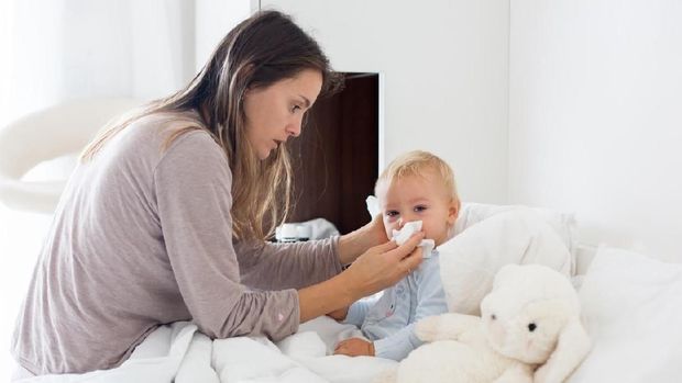 Mother and baby in pajamas, early in the morning, mom taking care of her sick toddler boy. Baby in bed with fever and running nose