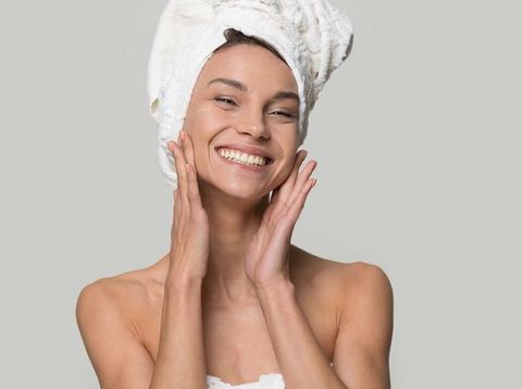 Studio portrait over grey perfect woman with white towel on head after shower having toothy smile touch gently healthy shiny clean skin looking at camera, skincare and natural beauty treatment concept