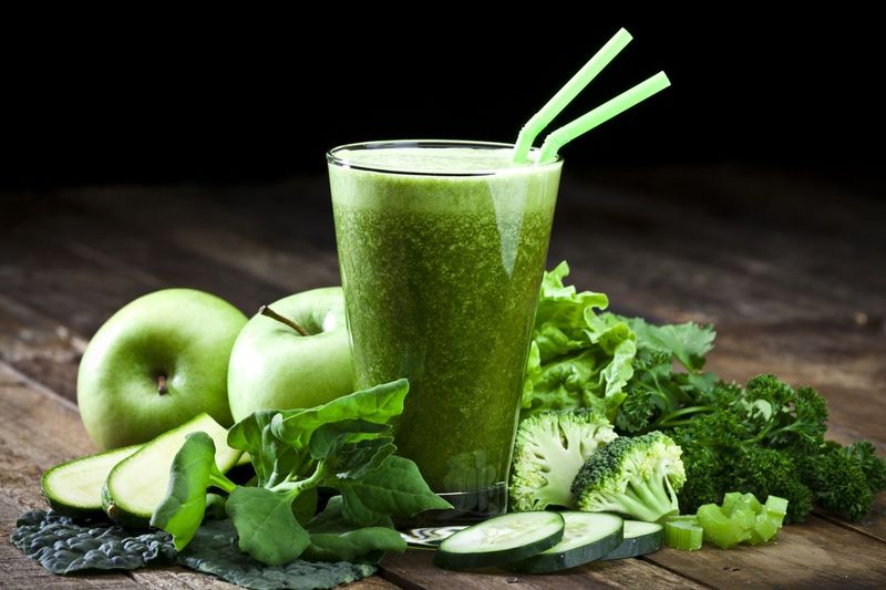 Glass of fresh green vegetable juice with two drinking straws on rustic wood table. The glass is surrounded by green vegetables like spinach, lettuce, broccoli, celery, green apples, parsley and cucumber. This is a drink used for detox diet. Predominant colors are green and brown. DSRL studio photo taken with Canon EOS 5D Mk II and Canon EF 70-200mm f/2.8L IS II USM Telephoto Zoom Lens