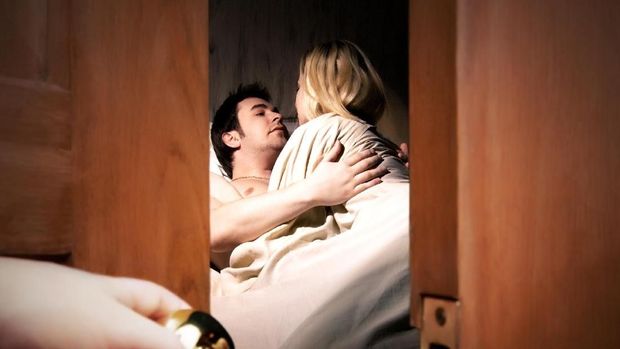 Couple lying in bed while someone is watching in front of the door