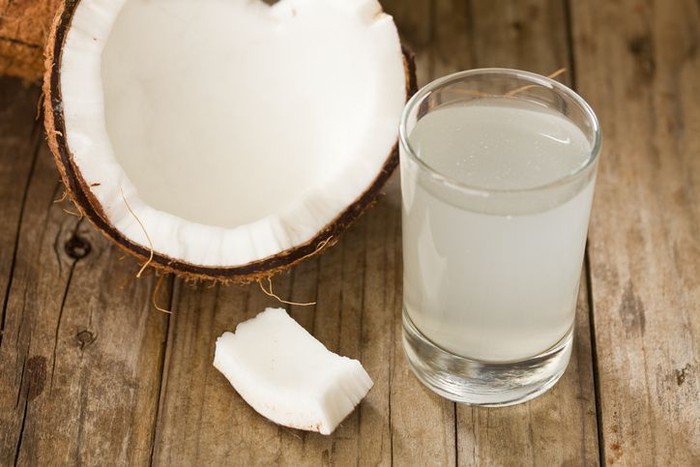 A high angle close up of half a coconut and a tumbler full of coconut water, coconut water is said to be rich in potassium and antioxidants. Shot on a grungy old wooden table.
