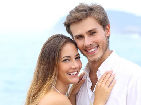 Front view portrait of a happy couple with perfect smile looking at you sititng on a couch in the living room at home in winter