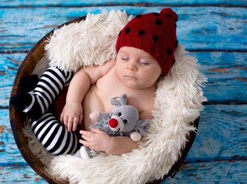 Little baby boy with knitted ladybug hat and pants in a basket, sleeping peacefully in a basket, isolated studio shot