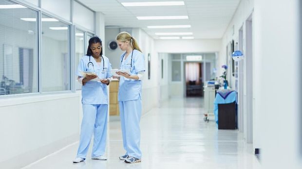 Full length of female nurses discussing medical documents in hospital corridor