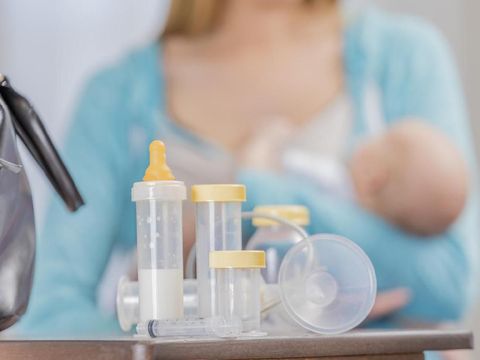 Close up of breastfeeding supplies. A mom holds a newborn in the background. The supplies are on a table along with a doctor's bag.