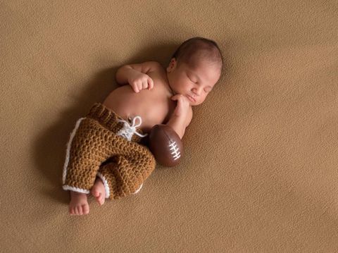 A sleeping, nine day old newborn baby boy wearing crocheted football uniform pants.