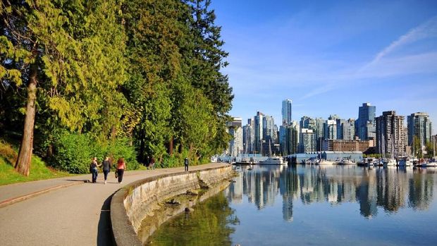 Vancouver, Ð¡anada - April 29, 2014: Stanley Park Seawall Path with pedestrians and cyclist, Vancouver waterfront marina and and modern condonimums and office towers are in the background