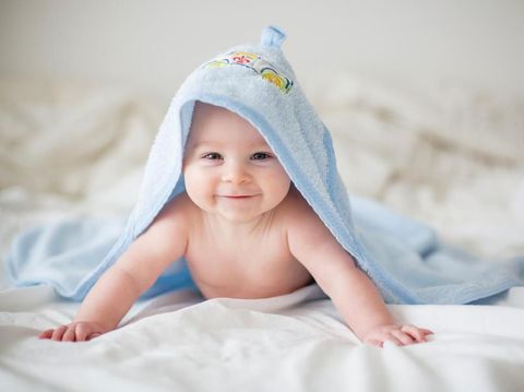 Cute little baby boy, relaxing in bed after bath, smiling happily, daytime