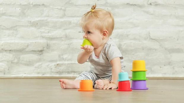 Baby girl playing on the floor with plastic educational   cups, early learning concept