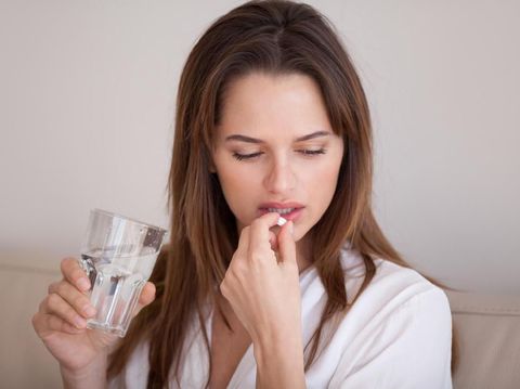 Sick young woman suffering from migraine or headache hold glass of water and painkiller medicine considering having pill, unwell millennial girl feel sad pondering taking antidepressant medication