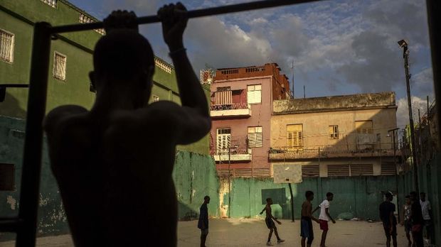 A young man exercises on a pull up bar near a pick-up soccer game, in Havana, Cuba, Wednesday, Feb. 5, 2020. (AP Photo/Ramon Espinosa)