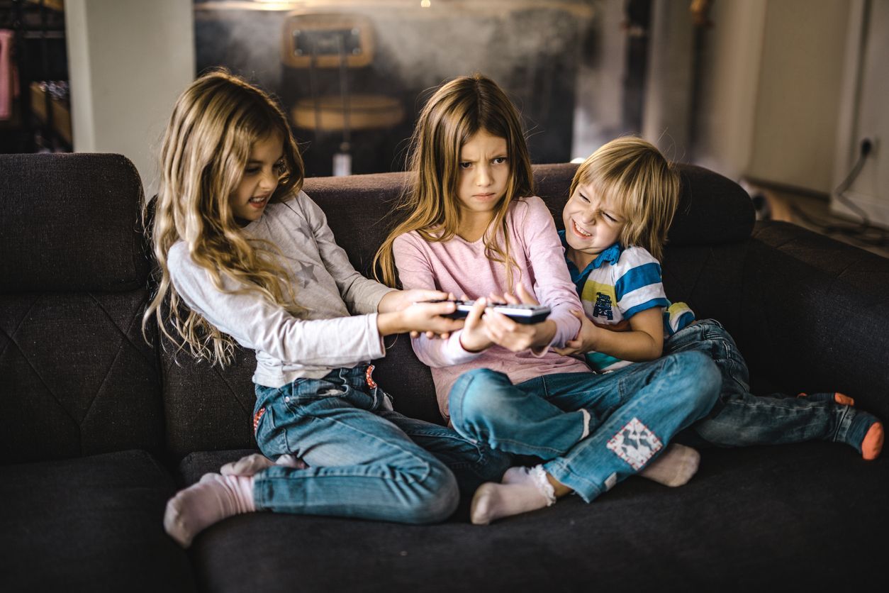 Angry little kids fighting over a remote control while watching TV on sofa at home.