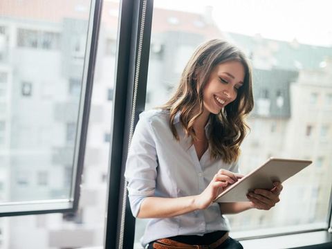 Young businesswoman using a digital tablet while standing in front of windows in office