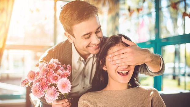 The happy man make a surprise with flowers for a girlfriend in the restaurant