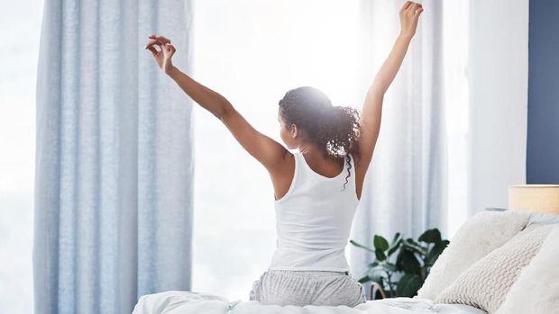 Rearview shot of an unrecognizable young woman stretching while sitting on her bed in the morning