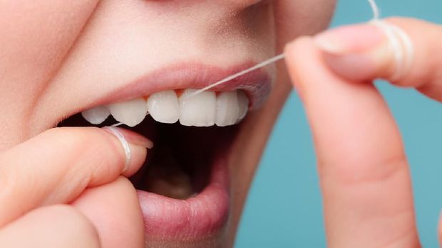 Portrait of a beautiful young woman flossing her teeth in the bathroom at home