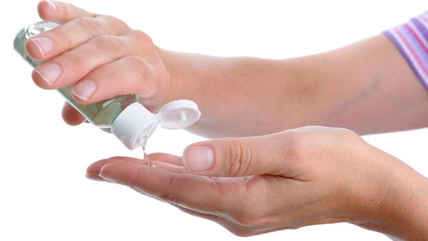 A woman's hand pouring alcohol-based hand sanitizer onto her other hand. Isolated against a white background.