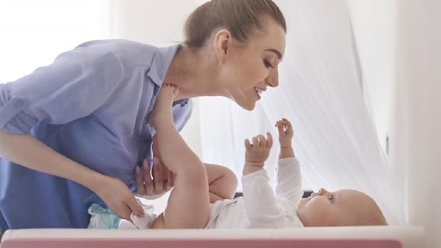 A smiling baby whose mother is changing a diaper