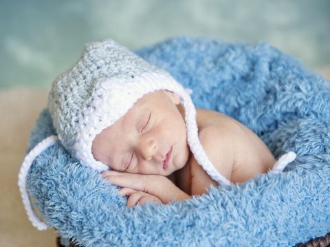A sleeping preemie newborn baby boy wearing a hat, studio shot, focus on face