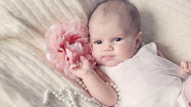 Newborn baby girl in fashionable dress with flower and pearl beads