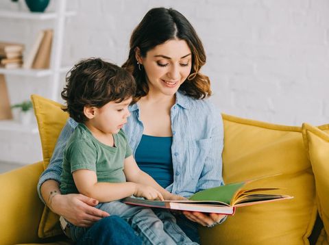 Mom and son sitting on yellow sofa and reading book