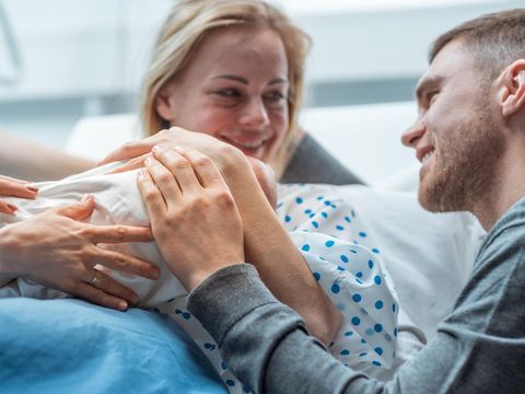 In the Hospital Midwife Gives Newborn Baby to a Mother to Hold, Supportive Father Lovingly Hugging Baby and Wife. Happy Family in the Modern Delivery Ward.