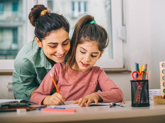 Happy family with kid playing together, caring mom and dad smiling teaching little daughter to draw with color pencils, mother and father having fun with cute child help in creative weekend activity