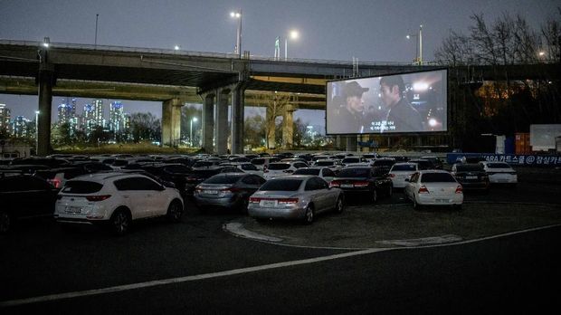 In a photo taken on March 21, 2020 an outdoor screen shows a movie at a drive-through cinema in Seoul. - Box office numbers in South Korea -- which has 8,897 confirmed virus cases -- have plummeted in recent weeks due to the epidemic, with authorities urging the public to avoid large crowds. But at drive-in cinemas, moviegoers can enjoy a movie from the comfort of their cars, parked in front of a large outdoor screen. (Photo by Ed JONES / AFP)