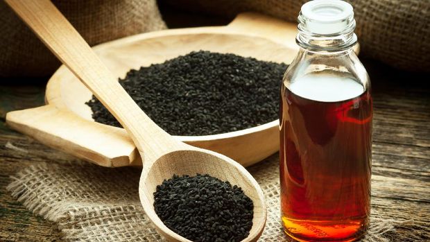 Nigella sativa (Black cumin) on wooden spoon and essential oil. Real oil from nigella looks like dark honey