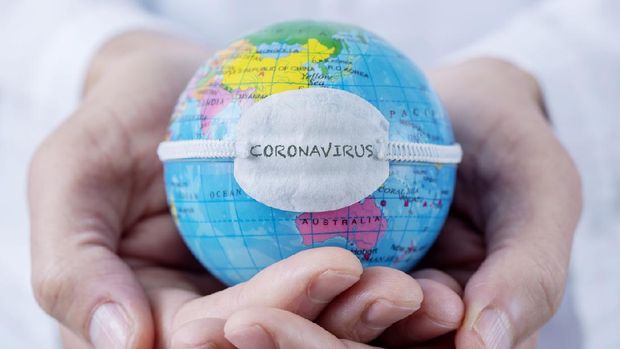 closeup of a caucasian doctor man holding a world globe with a protective mask with the word coronavirus written in it