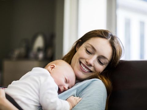 Young mother, holding her sick toddler boy, breastfeeding him at home, sunny living room