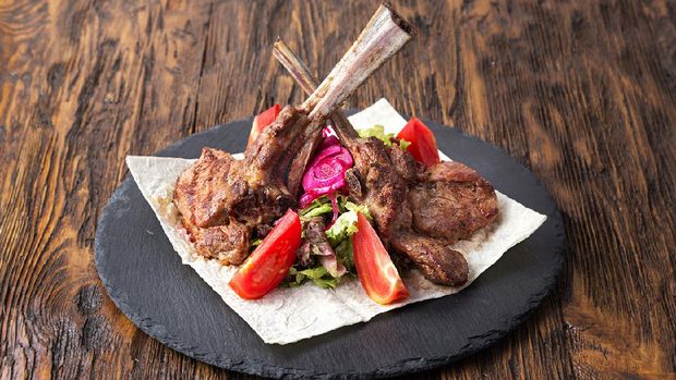 ribeye steak on the bone, tomahawk, served with tomatoes and iceberg lettuce on pita on slate board.