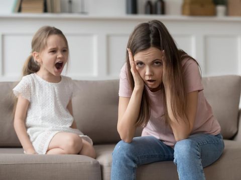 Stressed exhausted mother looking at camera feeling desperate about screaming stubborn kid daughter tantrum, upset annoyed mom tired of naughty difficult child girl misbehave yelling for attention