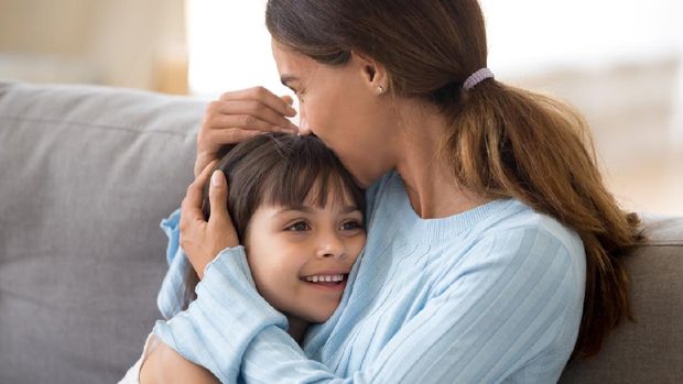 Loving single mother hugging cute little daughter kissing kid sitting on sofa, happy woman mum caressing embracing preschool girl, moms care and support, sincere warm relationships for child concept