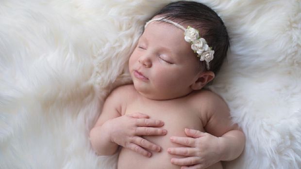 Sleeping, week old newborn baby girl wearing a paper rose headband. Shot in the studio on a white sheepskin rug.
