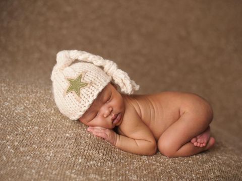 Cute newborn baby girl lying in the bed. 2 month old child in owl hat sleeping on blue blanket with stars