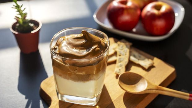 Es Kopi Dalgona Delicious homemade Iced Dalgona Coffee, a trendy fluffy creamy served on a table, with a plate of apple as background