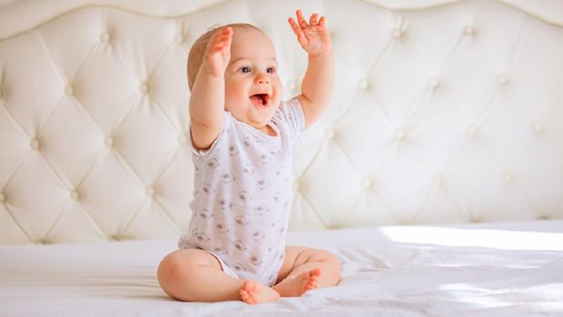 Cute baby boy in white sunny bedroom.