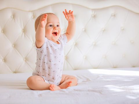 Cute baby boy in white sunny bedroom.