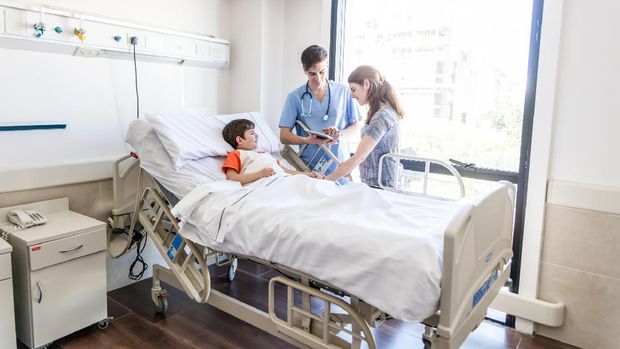 Friendly male pediatrician showing the test results to mother while boy is lying down on hospital bed all smiling