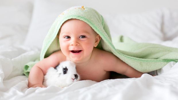 Cute little baby boy with little rabbit in bed after bath, baby after shower, cute child smiling at camera, bunny hext to  him