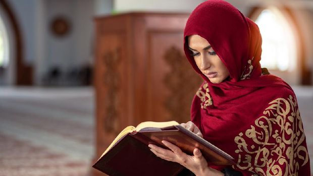 Young Muslim woman praying in mosque with Quran.